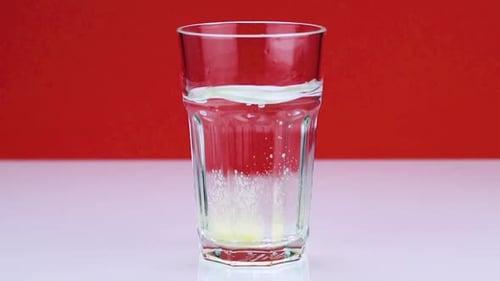 An Effervescent Pill Against Pain Falls Into a Glass and Dissolves Slow-motion Shot of Aspirin on a