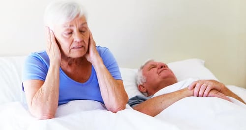 Femme irritée se couvrant les oreilles tandis que l'homme ronflait sur le lit