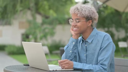 Young African Woman Doing Video Chat on Laptop in Outdoor Cafe