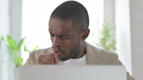 Close Up of African Man Coughing While Using Laptop
