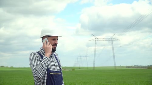 Engineer on Phone in Field by Power Lines