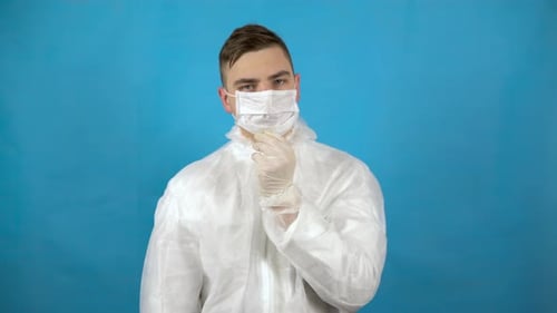 A Young Man Is Wearing a Protective Suit. A Man Puts on a Mask, Glasses and a Hood on a Blue