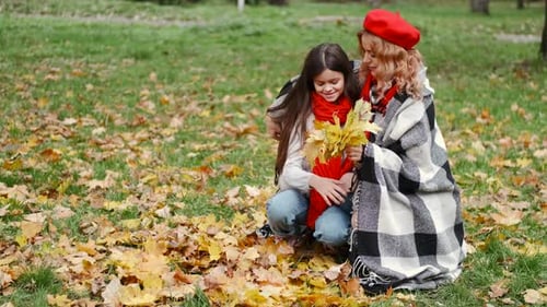 Mutter und ihre Tochter spielen mit fallenden Blättern im Herbstpark