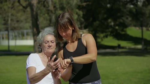 Two Women Comparing Time on Digital Devices in Summer Park
