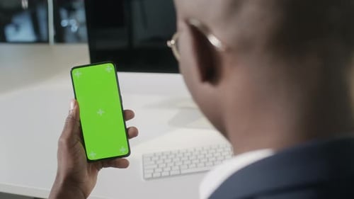 Young Adult Holding Smartphone with Green Screen in Office