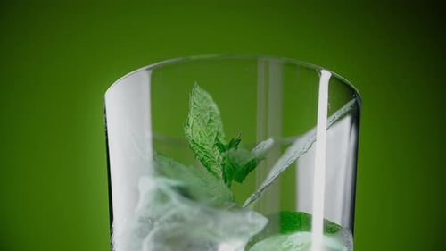 Leaf of Mint Drops to the Highbowl Glas mit Cocktail und Eiswürfeln auf grünem Hintergrund 1080p