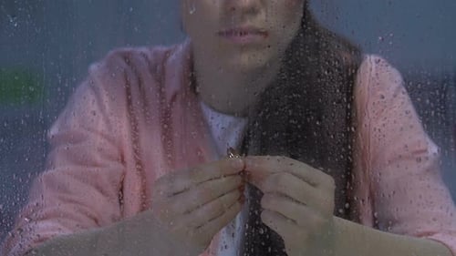 Sad Woman Holding Wedding Ring in Rainy Window