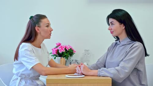 Two Young Women Holding Hands Talking Indoors