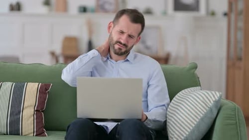 Man Using Laptop at Home Massages Neck