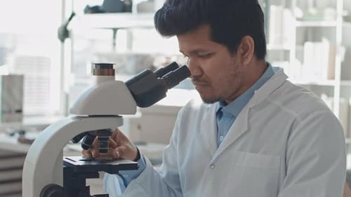 Biracial Male Engineer Looking at Computer Chip under Microscope