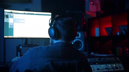 A Man Sound Engineer in Headphones Working in the Neon Sound Recording Studio