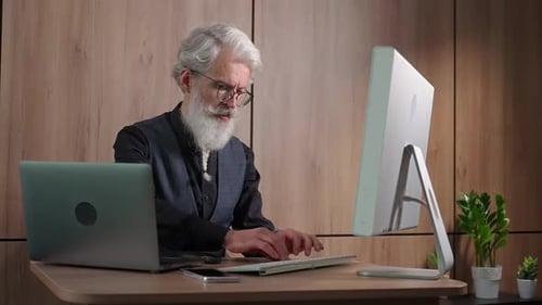 Un designer adulte aux cheveux gris travaille au bureau devant l'ordinateur en tapant et en surfant sur Internet