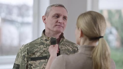 Woman Adjusts Collar of Man in Military Uniform