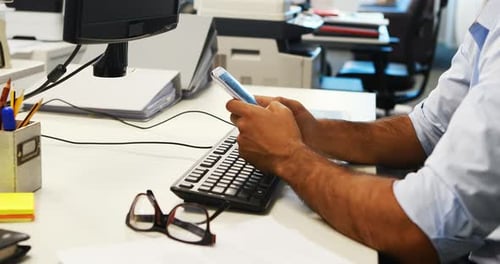 Cadre masculin utilisant un téléphone portable tout en travaillant sur un ordinateur
