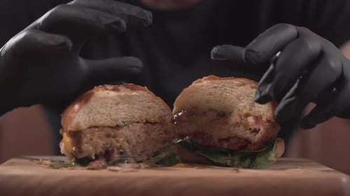 Manos masculinas con guantes negros tomando la mitad de la sabrosa hamburguesa de la tabla de madera