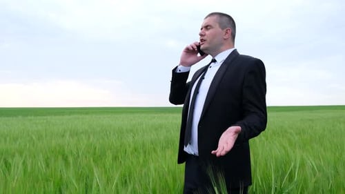 Angry businessman in the field talking on the phone.