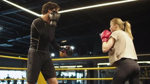 Smiling Coach Training with Female Athlete on Boxing Ring. Couple Boxing at Gym