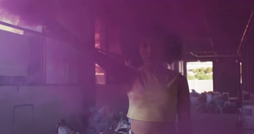 Mixed race woman holding purple flare standing in an empty building