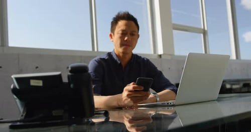 Asian business male executive using mobile phone at desk in office 4k
