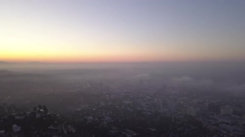AERIAL: Over Hollywood Hills at Sunrise with View on Los Angeles in Clouds