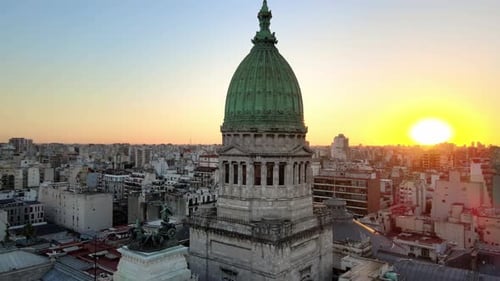 Órbita aérea alrededor del Congreso argentino que construye una torre de cúpula de bronce verde al atardecer en el barrio de Balvanera