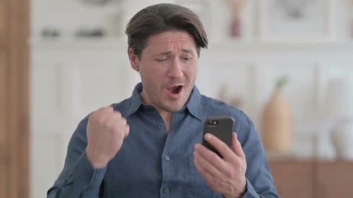 Man Celebrates Success Using Smartphone Indoors