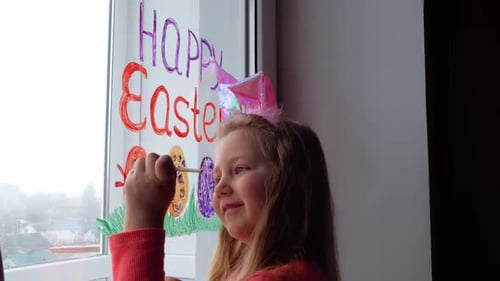 Cute little girl in bunny ears painting Easter eggs with green spring grass on window at home