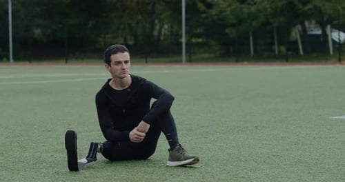 Male Disabled Sportsman with Prosthetic Running Blade Thinking While Sitting at Sports Field
