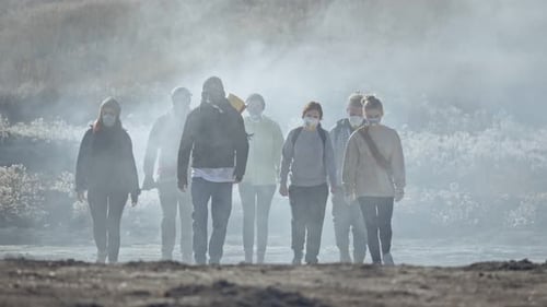 Gruppe junger Menschen in Gasmaske, die durch den giftigen Rauch in einer trostlosen und verbrannten Landschaft geht.