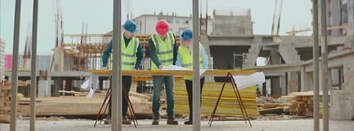 Three Construction Engineers Discuss Blueprint on Site