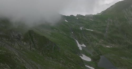Luftaufnahmen von Bergsee und Bergkette mit Schnee und Gipfeln in Wolken