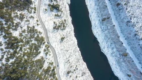 Cars Drive Snowy Road by River in Winter