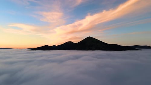 Vista aérea de uma grande montanha sobre nuvens brancas e densas ao nascer do sol.