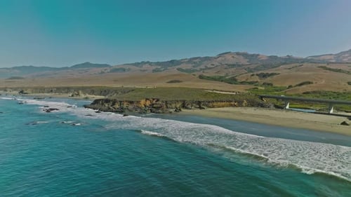 Aerial view of a road running between a mountain and the ocean