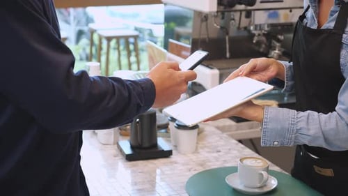 Hands of customer using smart phone scanning QR code for paying to cashier at cafe.