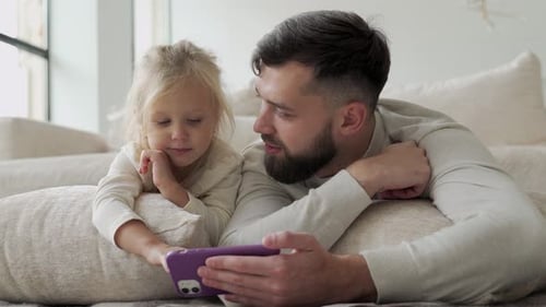 Dad and Daughter Watching a Cellphone Lying Down