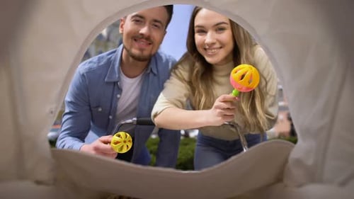 Cheerful Mom and Dad Shaking Rattle Toys Front of Newborn in Pram, Parenthood