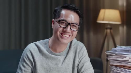 Close Up Of Asian Man Smiling To Camera While Working With Documents At Home