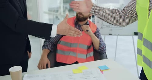 Hombre de traje apretando la mano con un ingeniero profesional experimentado en chaleco durante la reunión