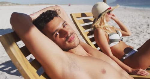 Caucasian couple sitting on sunbeds on the beach