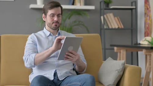 Man Uses Tablet While Sitting on Yellow Couch