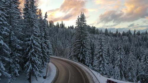 Aerial view of winter landscape with snow covered mountain hills and winding forest road in morning.