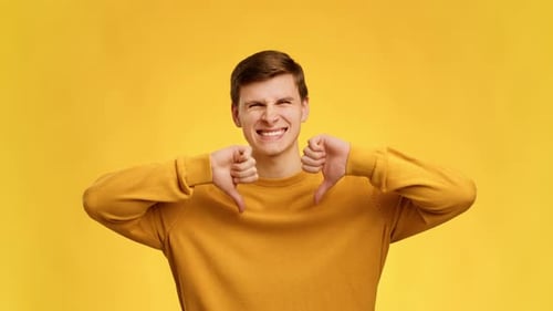 Displeased Man Gesturing Thumbs Down With Both Hands Yellow Background