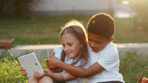 Children Share Tablet on Grassy Hill