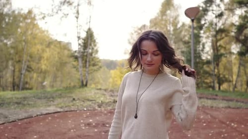 A Young Woman in a Sweater Walks in the Autumn Park. Brunette Woman Basks in the Cold Forest