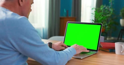Closeup of a Man Uses Laptop with Green Mockup Screen While Sitting at the Desk