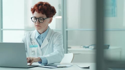 Young Female Doctor Working on Laptop and Taking Notes in Clinic