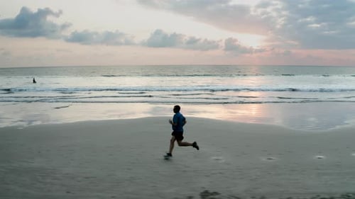 Tracking view of a runner on a tropical beach at sunset