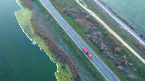 Aerial View of a Red Truck Driving Along a Dam Highway Surrounded By Lakes at Sunset