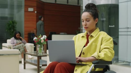 Woman Works on Laptop in Wheelchair in Office Lobby